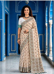 Woman wearing a beige saree with a pattern in front of a blue wall.