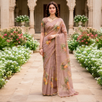 A woman stands in a garden courtyard wearing a dusty pink printed saree with a matching short-sleeve blouse. The saree has a floral pattern in muted green, orange, and yellow tones.