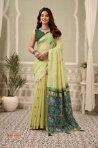 Woman wearing a light green saree with a patterned border indoors.
