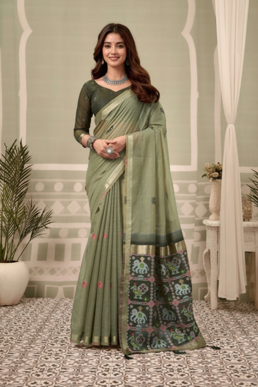 Woman in a green saree with a patterned border, standing in a decorative room.