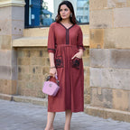 Woman in a red dress holding a pink handbag against a stone wall background