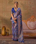 A two-panel catalog display showing a woman modeling a royal blue saree with intricate multicolor patterns. The left panel shows her standing, and the right panel shows her seated on an ornate gold chair.