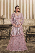 A woman models a traditional Indian outfit consisting of a heavily embellished light pink and silver sequined kurta with a matching dupatta, set against an ornate vintage interior background with striped wallpaper and a patterned sofa.