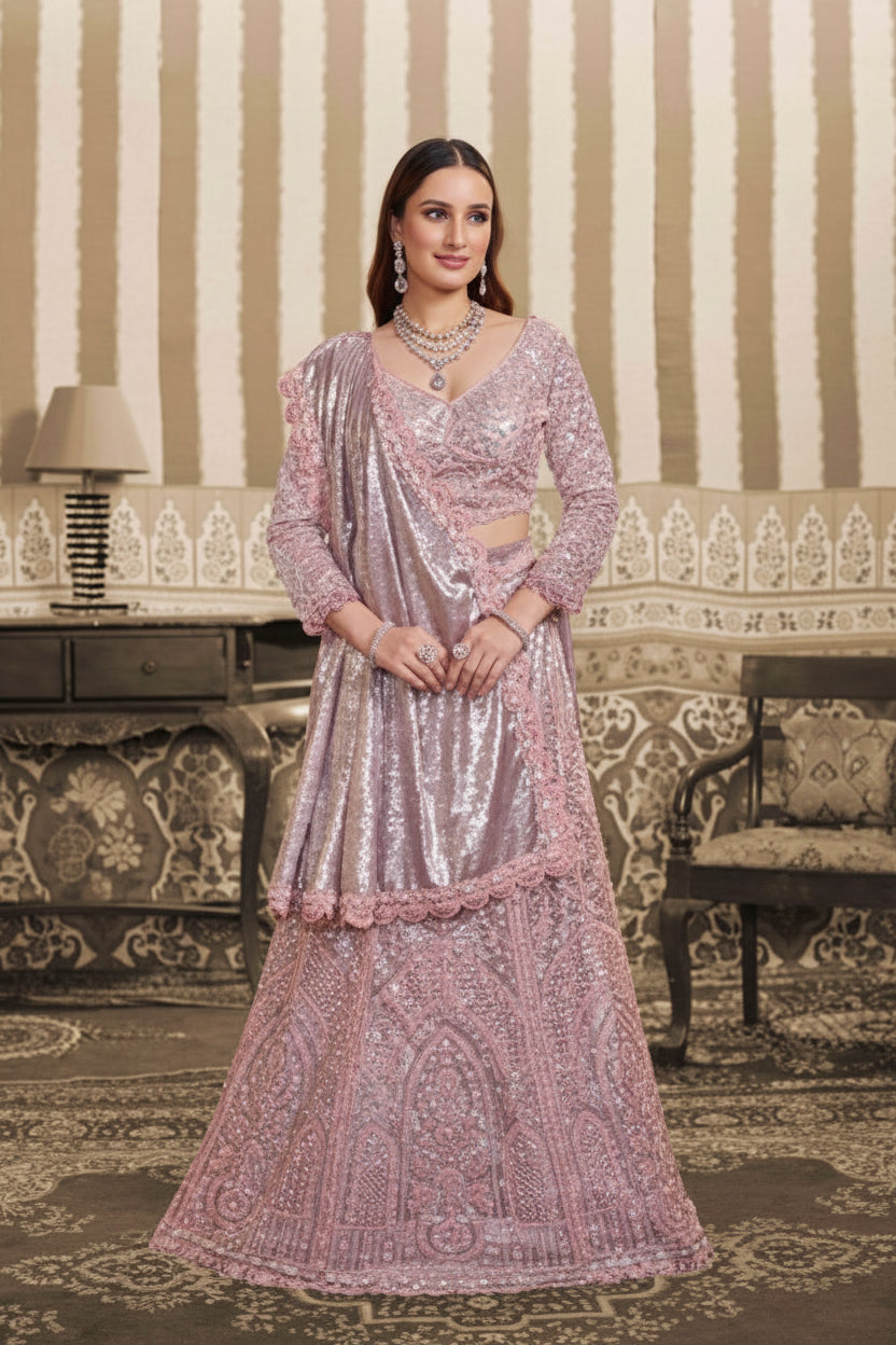 A woman models a traditional Indian outfit consisting of a heavily embellished light pink and silver sequined kurta with a matching dupatta, set against an ornate vintage interior background with striped wallpaper and a patterned sofa.