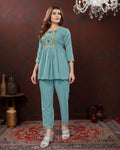 Woman wearing a teal outfit with embroidery in a room setting