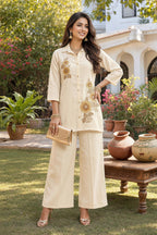 Woman in a beige traditional outfit with floral embroidery standing in a garden.