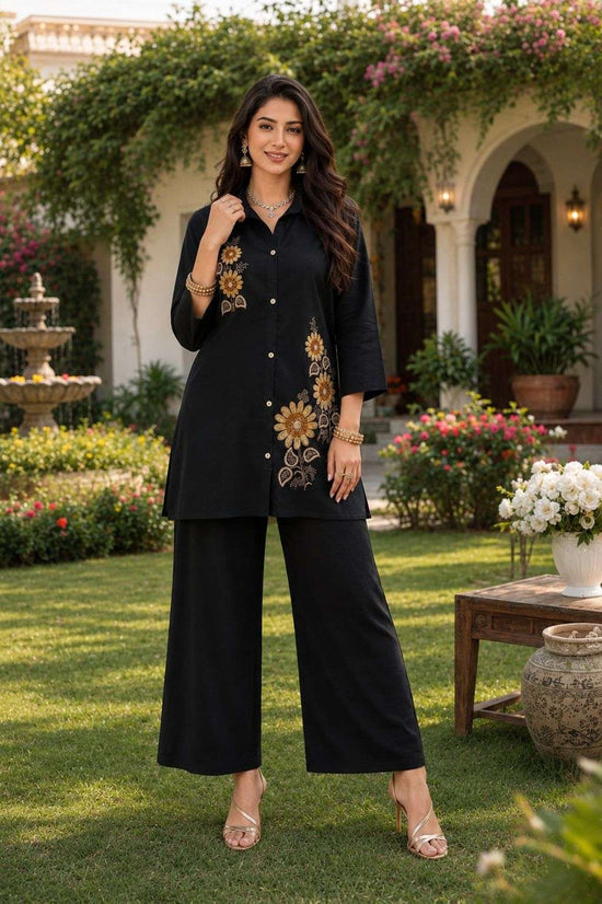 Woman in black embroidered outfit standing in a garden