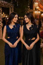 Two women in elegant blue and black dresses standing together at a formal event, with 'Nautanky' branding visible.