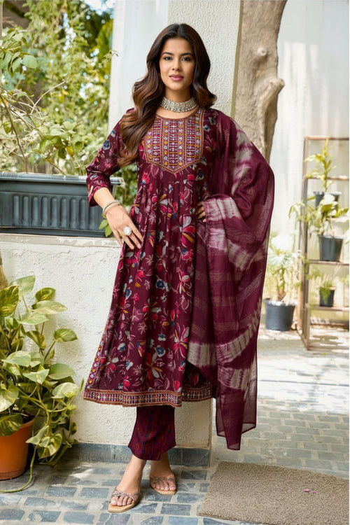 Woman wearing a maroon traditional outfit with a scarf, standing outdoors.