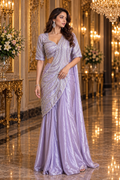 A woman models a lavender metallic saree with a matching embroidered blouse in an ornate, golden-lit hall.