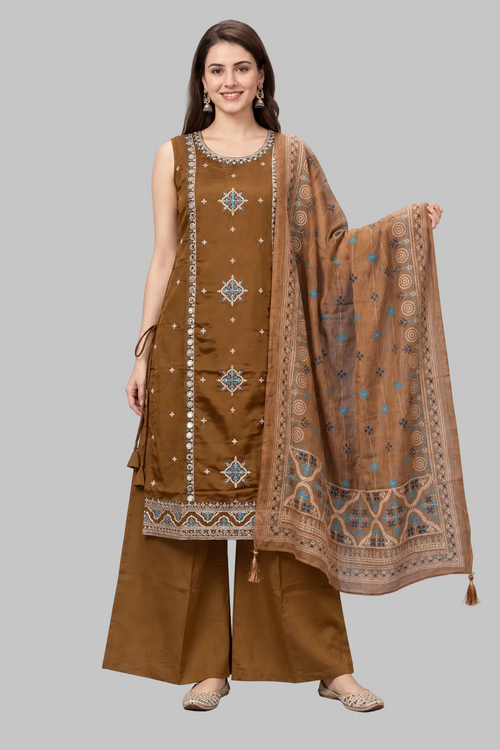 A woman modeling a traditional brown three-piece salwar kameez suit with a matching dupatta. The kurta features geometric embroidery in silver and blue, paired with wide-leg brown trousers and a brown dupatta decorated with blue and silver motifs.