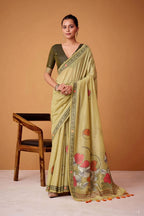 Woman wearing a light green saree with floral patterns, sitting on a chair against an orange background.