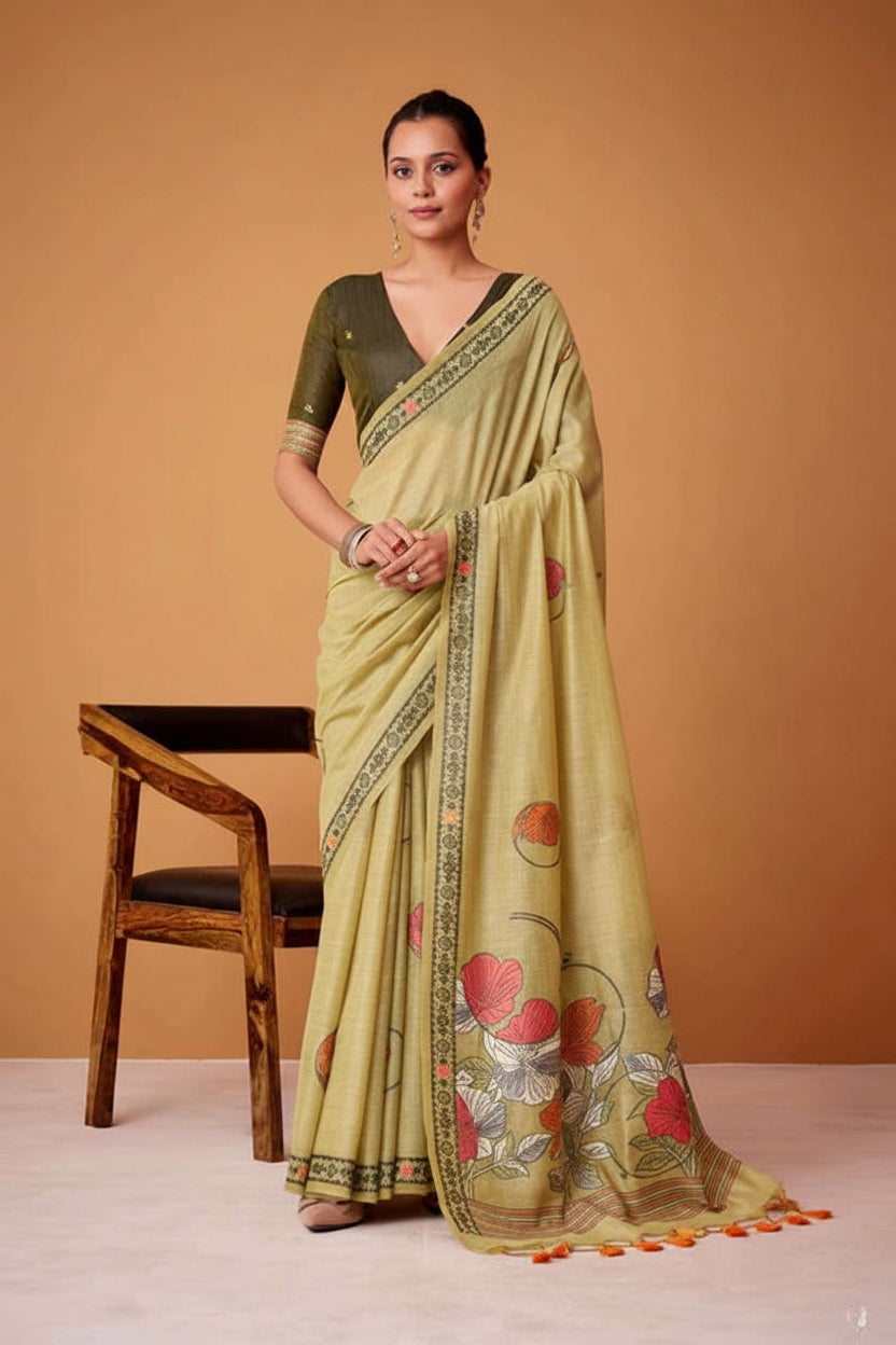 Woman wearing a light green saree with floral patterns, sitting on a chair against an orange background.