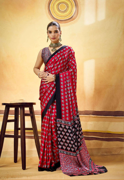 A woman models a red and black patterned saree with a purple embroidered blouse in a warm, beige-toned studio setting. The brand name Rajex is visible at the bottom left.
