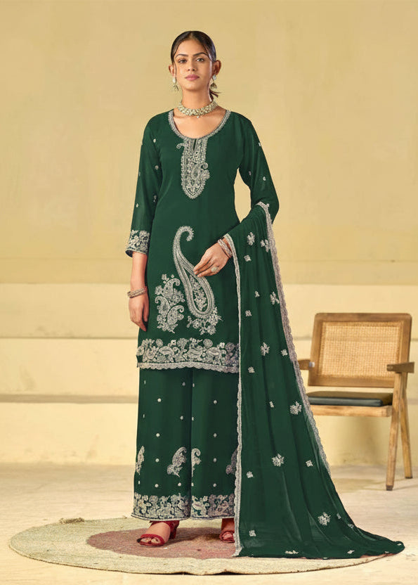 A woman models a dark green traditional Indian salwar kameez suit with white embroidery, featuring a kurta, wide-leg pants, and a dupatta. The image has a beige background with a wooden chair and the text 'Rangrut Khushi' in the top right corner.