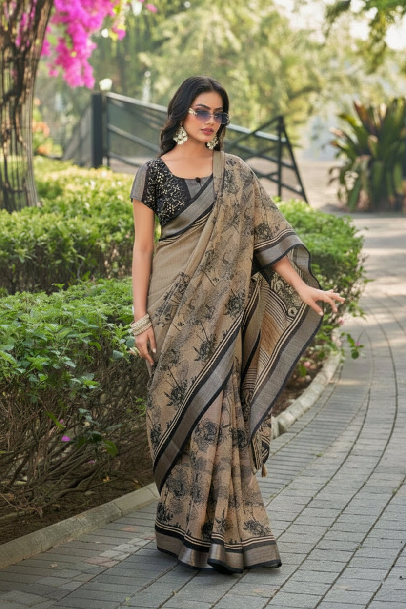 A woman wearing a beige and black printed saree with a black embroidered blouse, standing on a paved pathway in a garden setting.