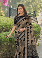 A woman wearing a black and beige geometric print saree with a black embroidered blouse, standing on a paved garden path.