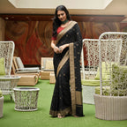 Woman in a black saree with gold border standing in an outdoor setting.