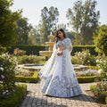 A woman modeling a white and blue printed ethnic lehenga choli set in a courtyard, shown in a split layout with a smaller inset view and the text '7079-WHITE' at the bottom.