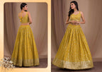 A woman modeling a yellow embroidered traditional Indian gown with a flared skirt and matching sleeveless top, shown in front and back views against a beige draped studio backdrop.